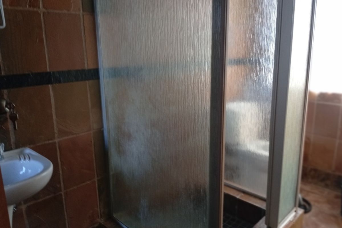 A dated bathroom featuring a shower enclosure and wall-mounted basin with terracotta-style wall tiling.