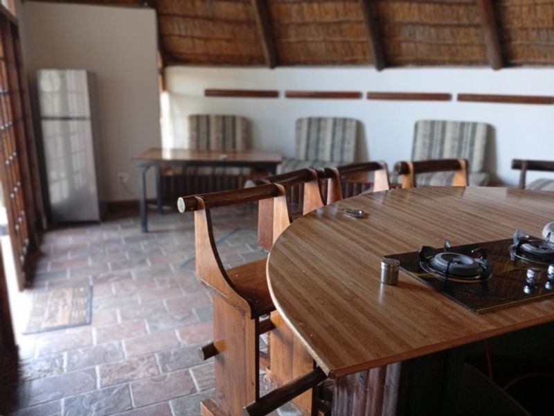 Open plan living area featuring a rustic thatched roof, stone tile flooring, and a built-in gas hob on a wooden counter.