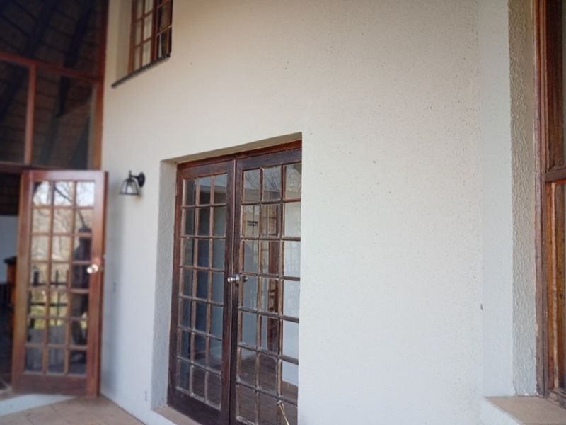 A covered patio area featuring wooden french doors and exterior wall lighting, providing access to the interior living space.
