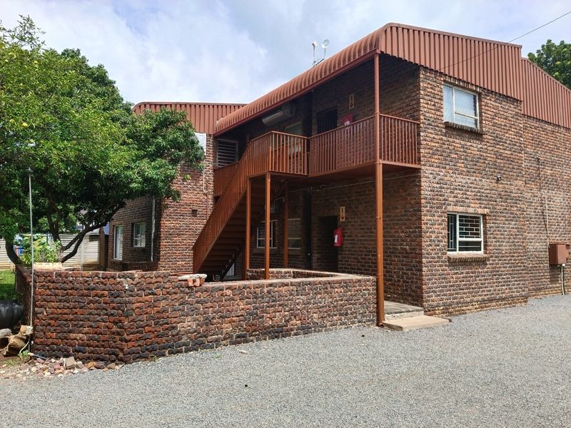 Exterior view of a multi-story face-brick apartment building featuring an external metal staircase, balcony access, and a low brick boundary wall.