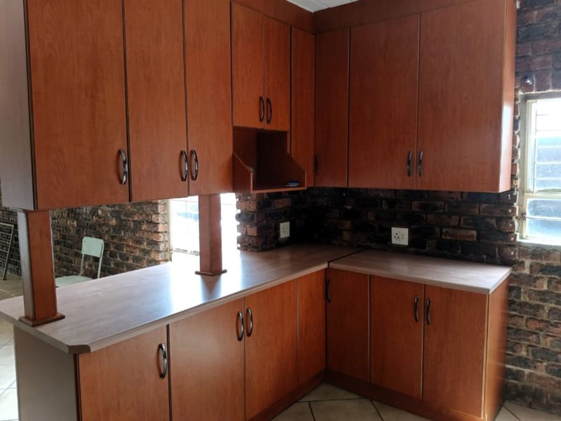 A kitchen featuring wooden cabinetry, laminate countertops, and an exposed brick wall, offering a rustic aesthetic ready for modernization.