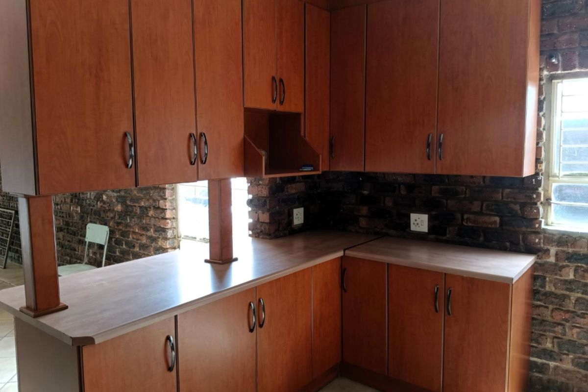 A kitchen featuring wooden cabinetry, laminate countertops, and an exposed brick wall, offering a rustic aesthetic ready for modernization.