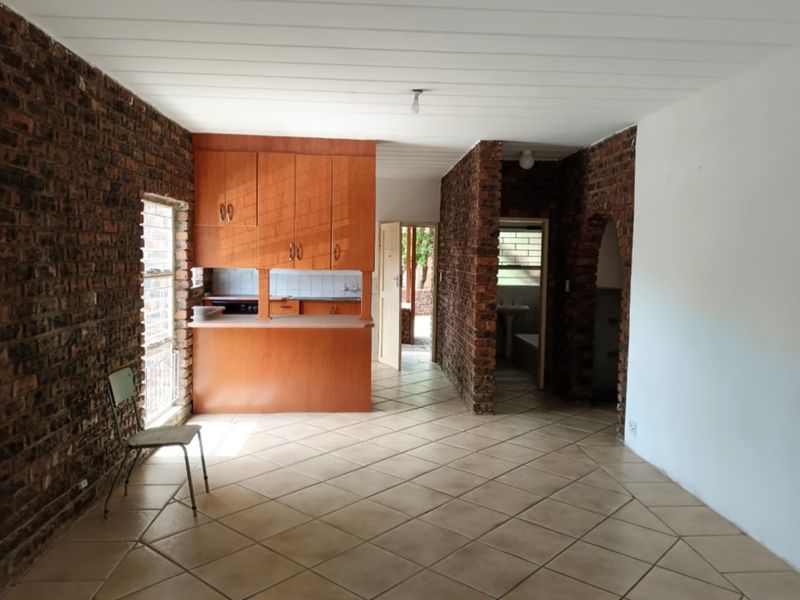 Open-plan living area featuring exposed brick walls, tiled flooring, and a functional kitchen with built-in cabinetry and a breakfast counter.