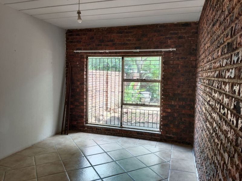 An empty bedroom featuring exposed brick walls, tiled flooring, and a window with security bars overlooking the exterior area.