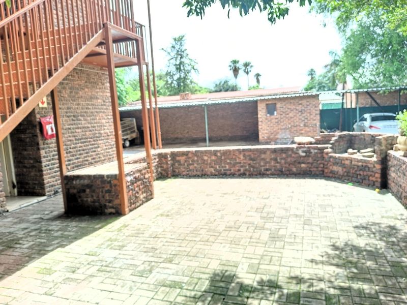 Rear exterior area featuring brick paving, a low brick retaining wall, and an external metal staircase leading to upper levels.