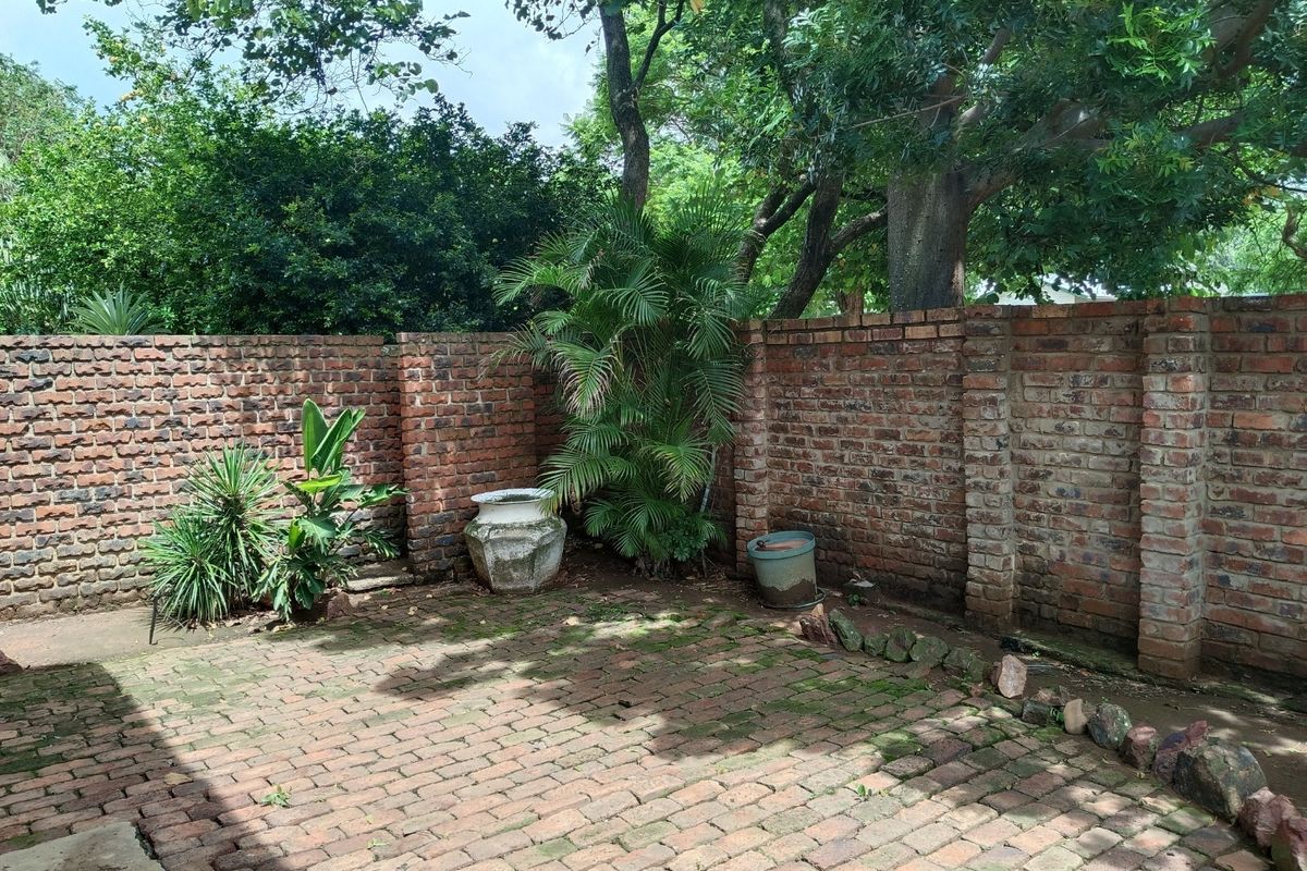 A private rear courtyard featuring a rustic brick paved patio enclosed by high brick boundary walls and mature garden trees.