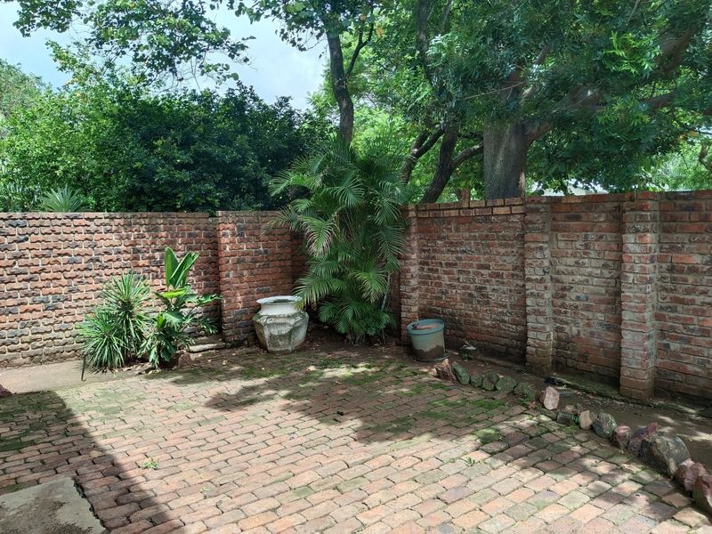 A private rear courtyard featuring a rustic brick paved patio enclosed by high brick boundary walls and mature garden trees.