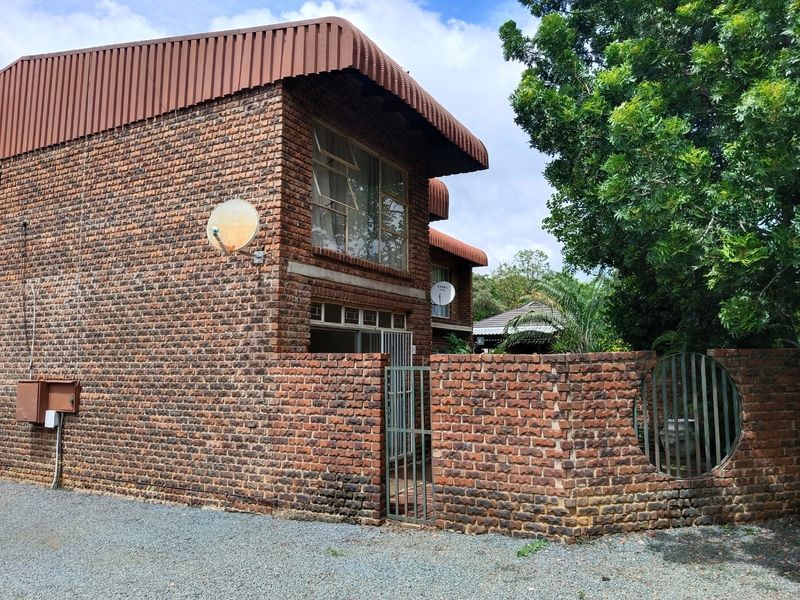 Exterior view of a two-story face brick apartment building featuring a metal roof awning, security gate, and a private brick-walled entrance area.