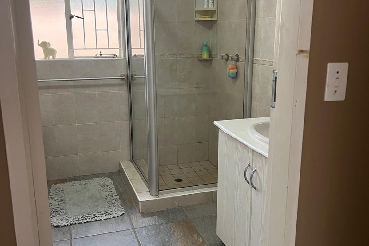 A functional bathroom featuring a corner shower enclosure, vanity cabinet, and neutral ceramic tiling throughout.