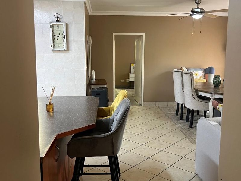 Open plan living and dining area featuring tiled flooring, a kitchen breakfast bar, and a ceiling fan, providing a functional layout for daily living.