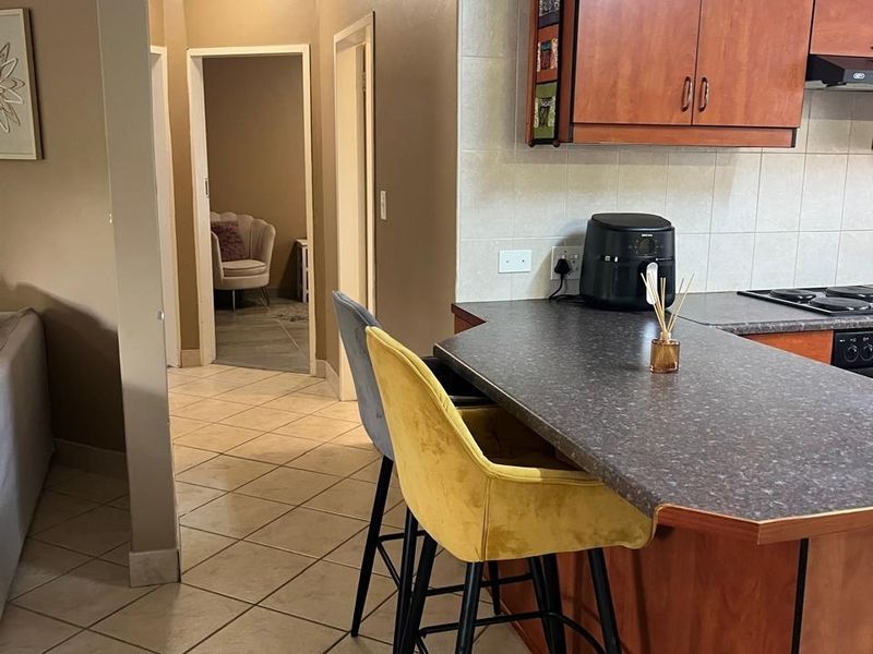 A functional kitchen area featuring wood-tone cabinetry, a dark laminate breakfast bar, and tiled flooring, leading into a hallway.