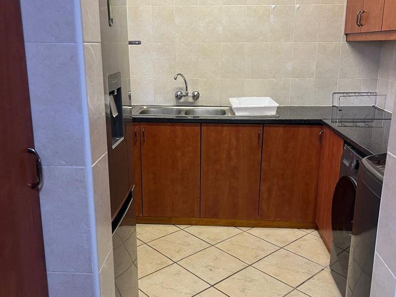 A functional laundry room featuring built-in wooden cabinetry, granite countertops, a double sink, and tiled finishes throughout.