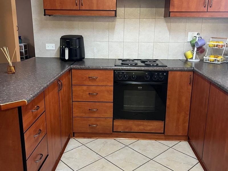 A functional kitchen featuring wooden cabinetry, laminate countertops, a built-in oven with electric hob, and tiled flooring.