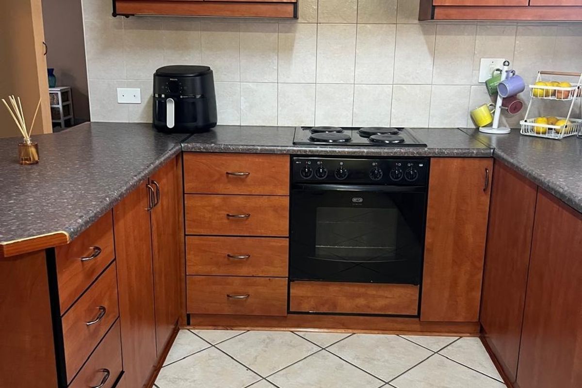 A functional kitchen featuring wooden cabinetry, laminate countertops, a built-in oven with electric hob, and tiled flooring.