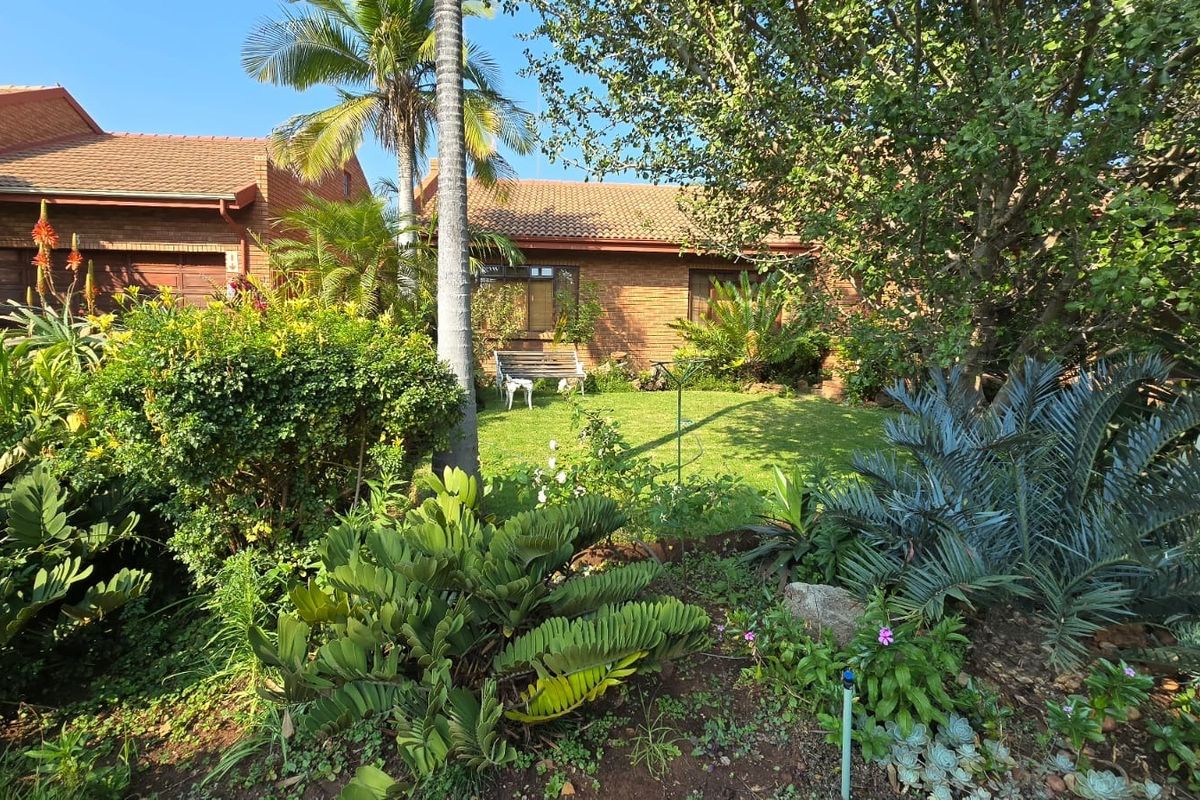 A view of the rear exterior of the townhouse, featuring a well-maintained brick facade, tiled roof, and a lush, established garden.