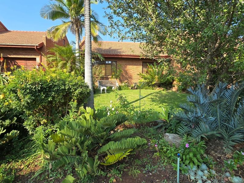 A view of the rear exterior of the townhouse, featuring a well-maintained brick facade, tiled roof, and a lush, established garden.