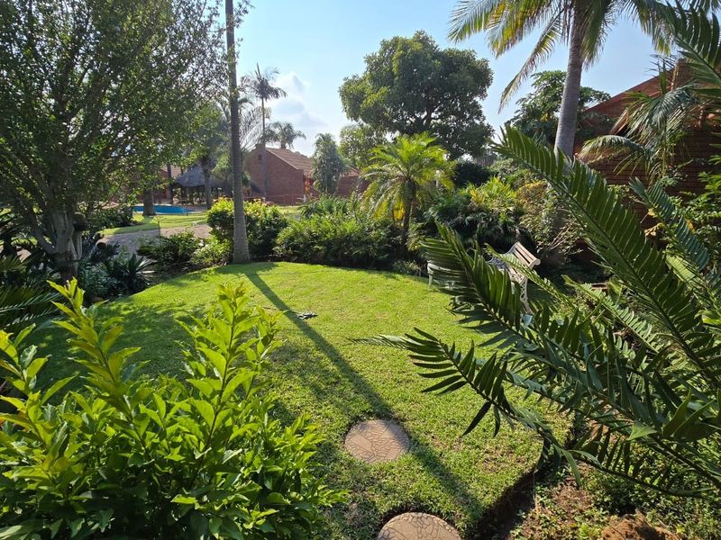 A well-maintained private garden featuring a lush green lawn, mature trees, and established landscaping within a townhouse complex.