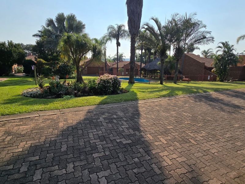 A view of the rear exterior featuring a paved driveway, landscaped garden, and a swimming pool area surrounded by brick townhouse units.