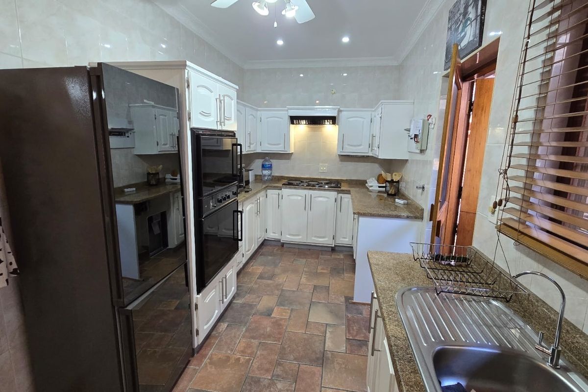 A functional kitchen featuring white cabinetry, granite countertops, a built-in oven, gas hob, and tiled flooring with a double sink area.