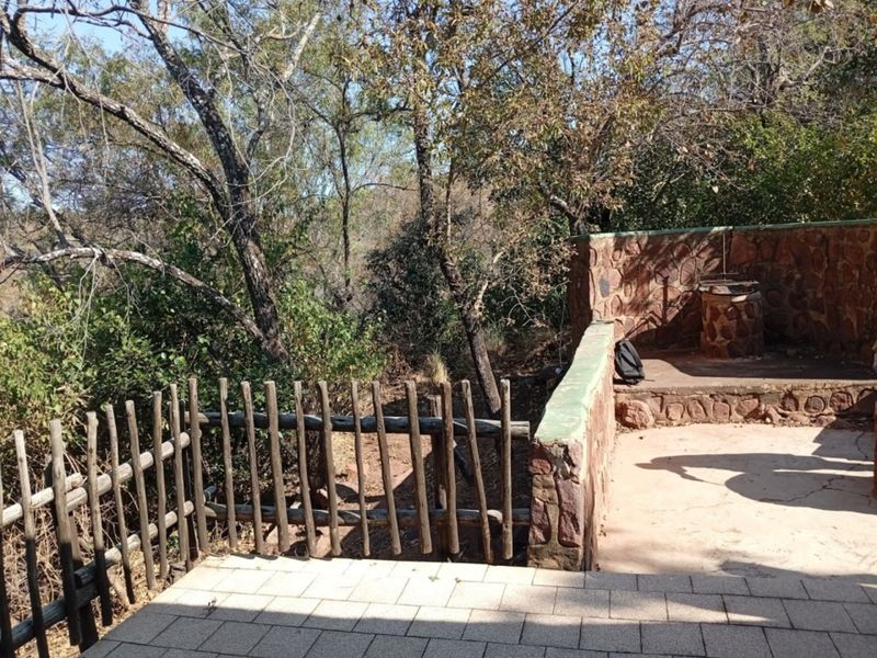 Outdoor patio area featuring a stone masonry wall, built-in braai, and timber fencing, overlooking a natural wooded landscape.