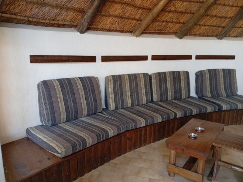 A rustic living area featuring a built-in wooden bench, traditional thatched roof with exposed timber rafters, and tiled flooring.