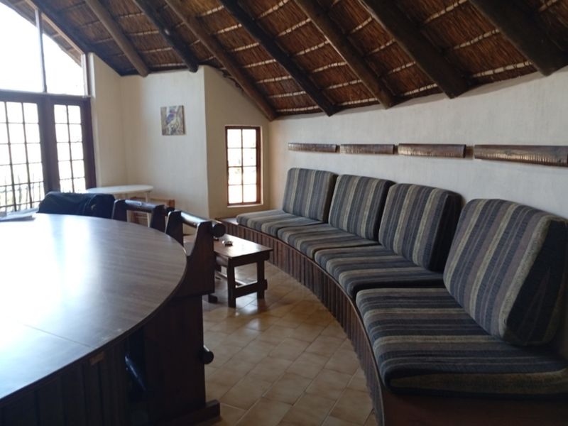 Spacious living area featuring a unique thatched roof with exposed timber rafters, built-in bench seating, and large windows providing natural light.