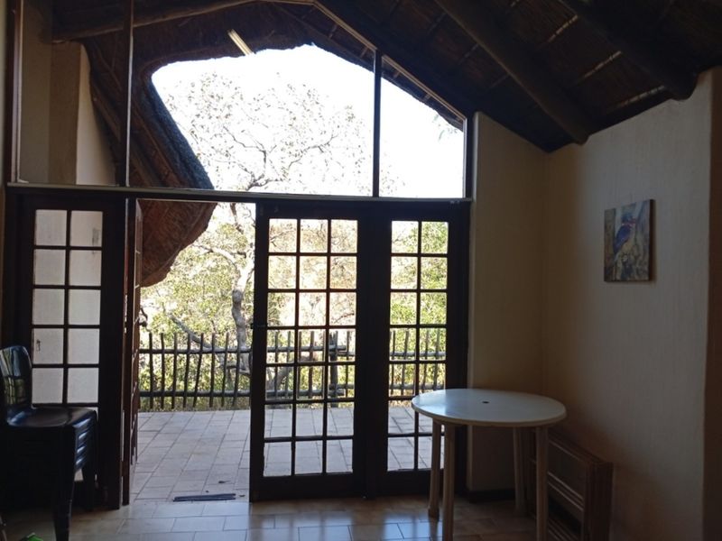 Living area featuring a vaulted thatched roof with exposed rafters, tiled floors, and large timber-framed glass doors opening onto an outdoor patio.