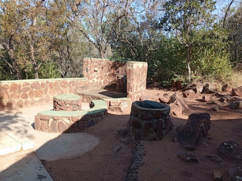 Outdoor rear entertainment area featuring rustic stone masonry walls, built-in stone seating, and a built-in braai facility set within a natural garden landscape.