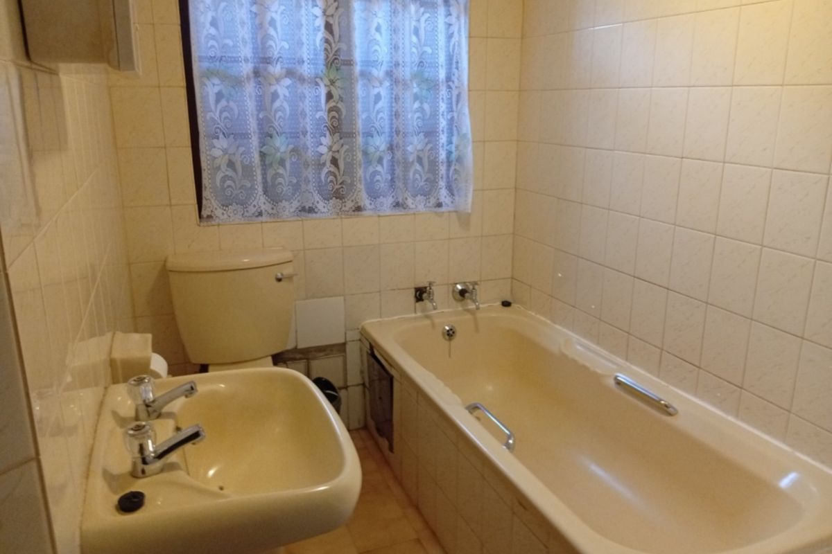 A dated bathroom featuring a pedestal basin, bathtub, and toilet with original ceramic wall tiling and flooring.