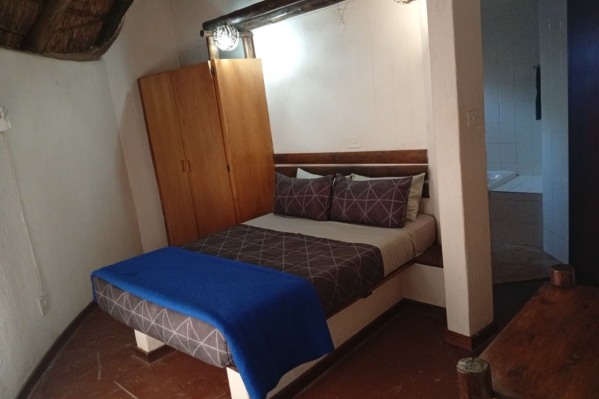 A bedroom featuring a thatched roof, exposed timber beam, built-in wardrobe, and direct access to an en-suite bathroom.