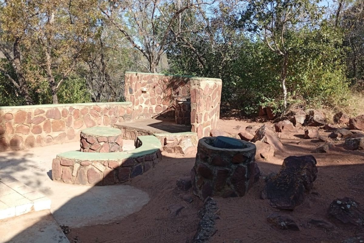 Outdoor rear entertainment area featuring rustic stone masonry walls, built-in stone seating, and a built-in braai facility set within a natural garden landscape.