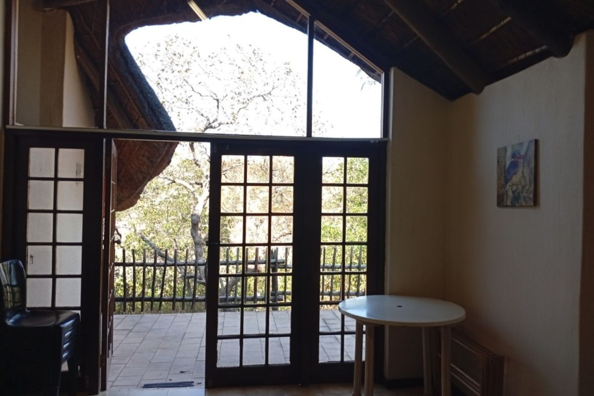 Living area featuring a vaulted thatched roof with exposed rafters, tiled floors, and large timber-framed glass doors opening onto an outdoor patio.
