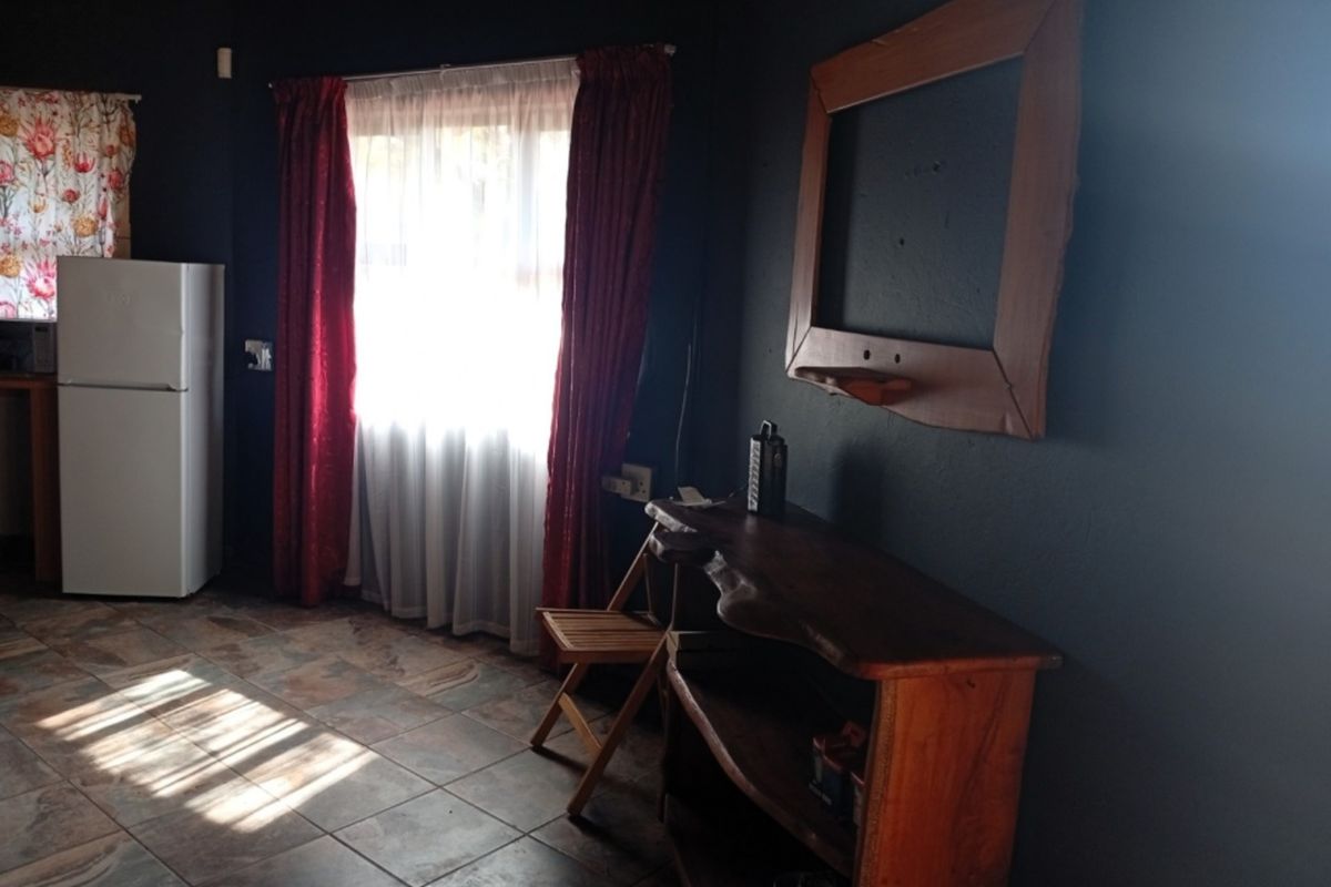 A living area featuring dark painted walls, tiled flooring, and a window with curtains, providing a functional space with potential for modernization.