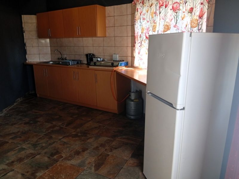 A functional kitchen featuring laminate cabinetry, tiled backsplash, stainless steel sink, and a gas hob, with stone-look floor tiles throughout.
