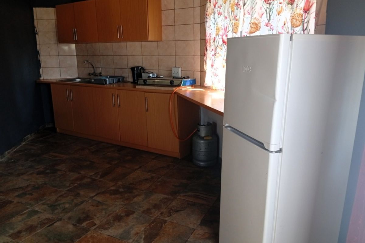 A functional kitchen featuring laminate cabinetry, tiled backsplash, stainless steel sink, and a gas hob, with stone-look floor tiles throughout.
