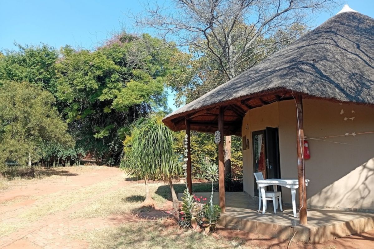 A view of a rustic unit featuring a traditional thatched roof and a covered patio area set within a natural, wooded environment.