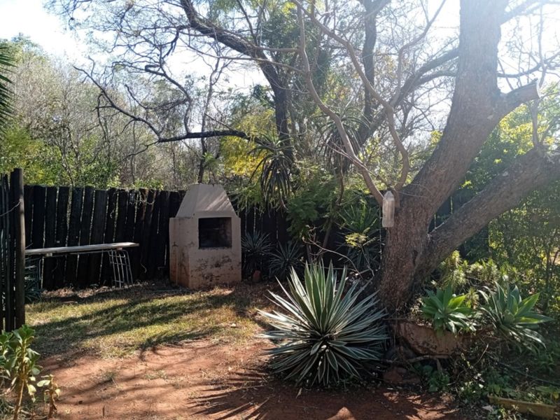 A private garden area featuring a built-in braai and established trees, enclosed by a timber fence.