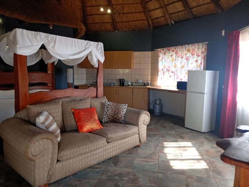 Open-plan living area featuring a high thatched ceiling, tiled flooring, and a compact kitchenette with built-in cabinetry.