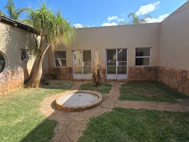 A private rear courtyard featuring a stone-clad wall base, paved pathways, and a central garden feature, providing direct access to the home's interior.