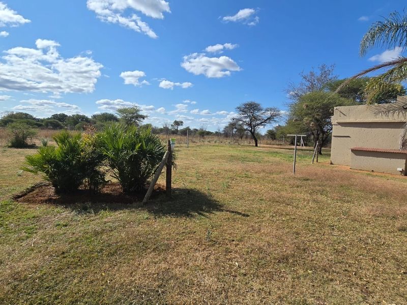 A spacious, open garden area featuring a grass lawn, established shrubs, and a clothesline, adjacent to the exterior wall of the property.