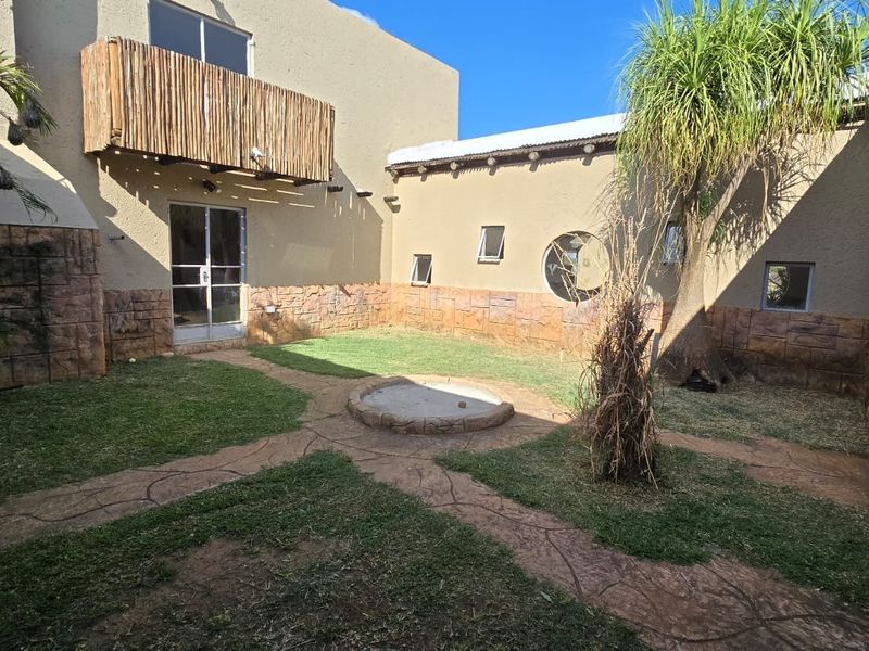 A private rear courtyard featuring stone-clad walls, a small balcony, paved pathways, and a central built-in fire pit area.