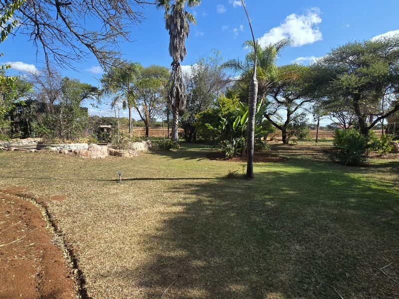 A spacious, well-established garden featuring mature trees, landscaped areas, and natural rock features, offering a peaceful outdoor setting.