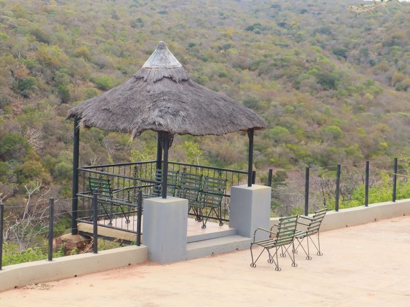 Outdoor terrace featuring a thatched roof gazebo and metal balustrade, offering elevated views of the surrounding natural landscape.