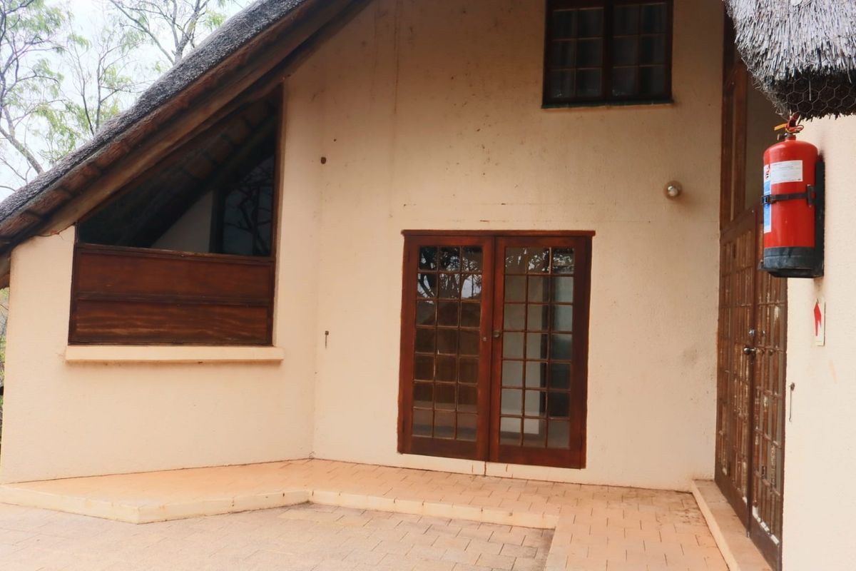 Rear exterior view of the apartment featuring a thatched roof, paved patio area, and timber-framed glass doors providing access to the interior.