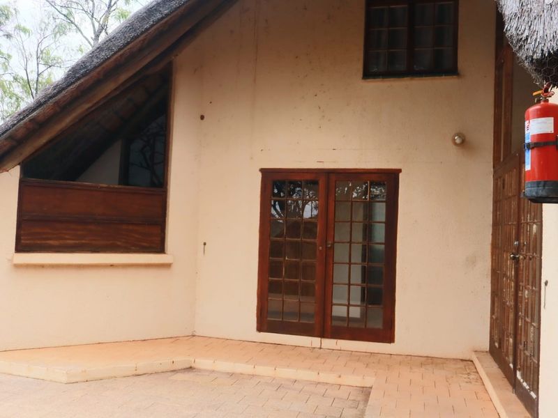 Rear exterior view of the apartment featuring a thatched roof, paved patio area, and timber-framed glass doors providing access to the interior.