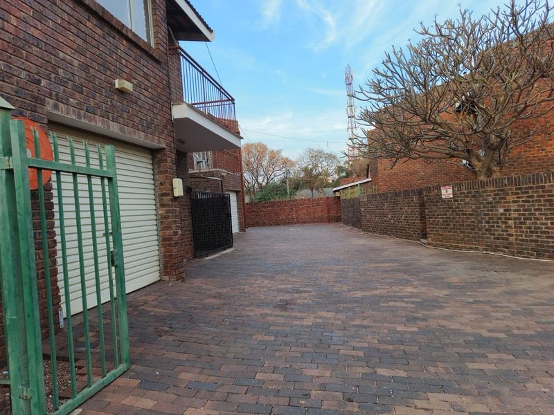 Exterior view of an apartment complex featuring a paved driveway, brick facade, and secure gated access with roller garage doors.