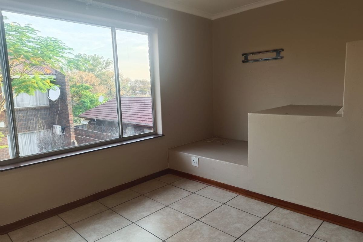 An empty bedroom featuring tiled flooring, a large window providing natural light, and a unique built-in masonry platform suitable for a bed base.