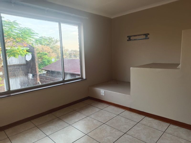 An empty bedroom featuring tiled flooring, a large window providing natural light, and a unique built-in masonry platform suitable for a bed base.