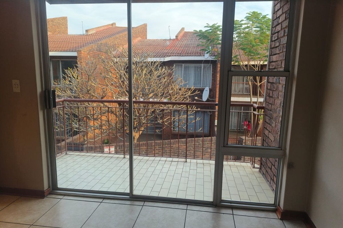 A view from an interior space through a large sliding glass door onto a tiled balcony with a metal balustrade and brick exterior wall.