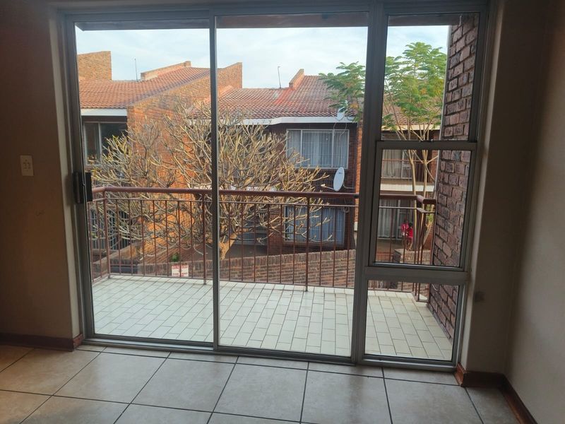 A view from an interior space through a large sliding glass door onto a tiled balcony with a metal balustrade and brick exterior wall.